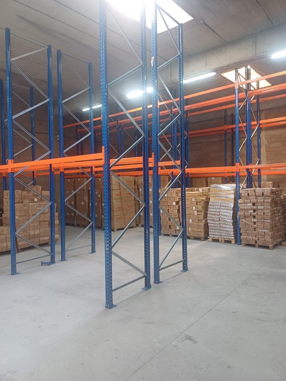 Racks à palettes bleus et orange installés par ARCOSTE dans un entrepôt, avec des palettes de cartons